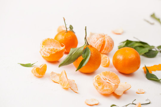 Peeled tangerines and peel with leaves on white background