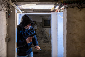 ein Einbrecher mit Pistole und Brecheisen dringt in einen alten Keller ein