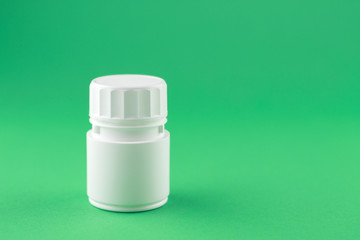 Close up white pill bottle on jade green background with copy space. Focus on foreground, soft bokeh. Pharmacy drugstore concept