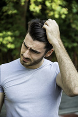 Confused or doubtful young man scratching his head and looking down. Outoodr on the street