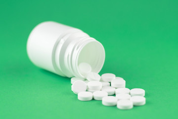 Close up white pill bottle with spilled out pills on jade green background with copy space. Focus on foreground, soft bokeh. Pharmacy drugstore concept