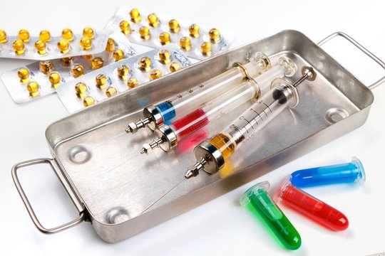 Syringes with medication in sterilization box, blister packs and vials with fluid on white surface