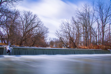 Long exposure exterior daytime stock photo of waterfall and felled log with blue sky background in...