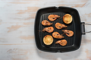 Grilled shrimps on a grill frying pan with lemon, paprika, spices and herbs. Wooden background.