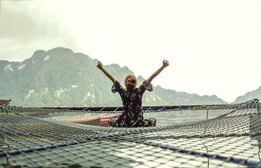 Fototapeta na wymiar Young female sitting on the net floor in freedom time looking to lake and mountain background
