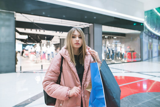 Stylish blonde woman with shopping in her hands is standing on the background of a clothing store. Shopping concept