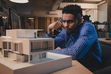 Young confident African American black male architect working on a private house project in the office, studying mansion model