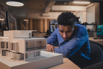 Young confident African American black male architect working on a private house project in the office, studying mansion model
