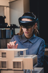 Young confident Caucasian female architect working on a private house project in the office using augmented reality glasses