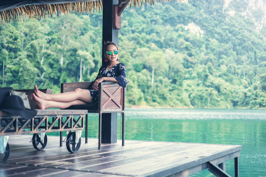 Beautiful woman in blue dress wear sunglass sit on lounge chair at lake and mountain. Luxury vacation. relax in weekend concept