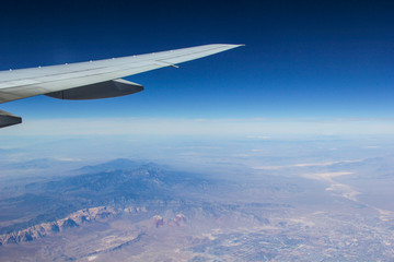Fototapeta premium The view from a plane of the wing and the ground below with blue skies