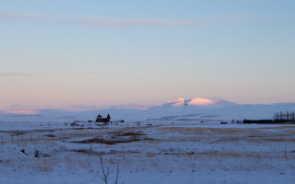 Frozen snowy landscape with snow covered mountains in Iceland at sunrise/sunset with golden hour glow.