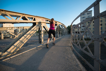 woman jogging across the bridge at sunny morning