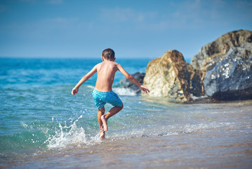 Cute Caucasian boy is running in the water along the sea shore.