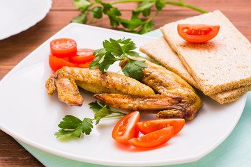 Baked chicken wings with cherry tomatoes, greens and bread on a plate