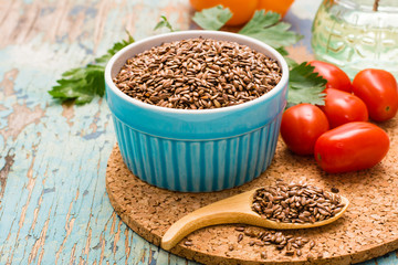 Flax seeds in a spoon and a bowl, fresh vegetables on a wooden table. Control over excess weight