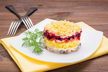 Traditional Russian salad - herring under a fur coat in a plate on a wooden table