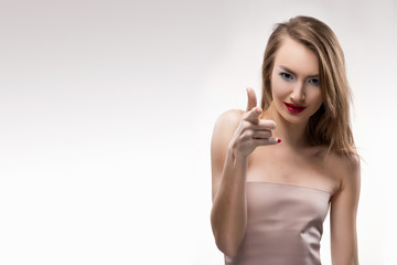 Fototapeta premium The beautiful blonde red lips smiling girl points finger to you (the viewer).