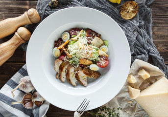 fclassic Caesar salad with quail eggs and chicken on a white plate on a wooden table