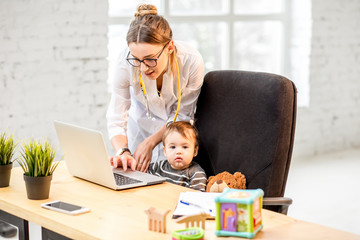 Nurse examining health of a baby boy playing on the laptop in the office