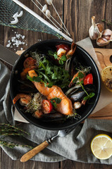 a seafood pan with baked salmon, shrimps and mussels with lemon on a wooden table with a glass of wine on a wooden table