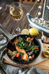 a seafood pan with baked salmon, shrimps and mussels with lemon on a wooden table with a glass of wine on a wooden table