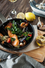 a seafood pan with baked salmon, shrimps and mussels with lemon on a wooden table with a glass of wine on a wooden table