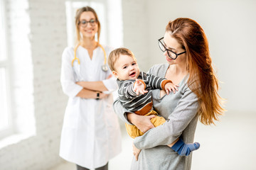 Portrait of a young woman pediatrician with mother and her baby boy at the white office