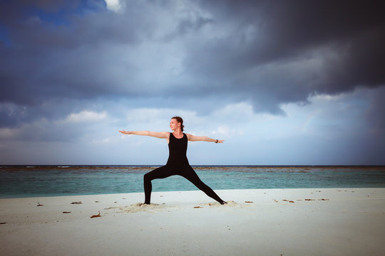 young girl standing in yoga warrior asana on dreamlike beach on summer vacation