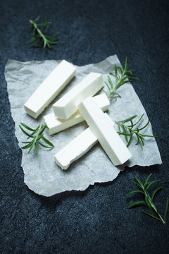 Portion of feta cheese with rosemary on a black background, vertically.