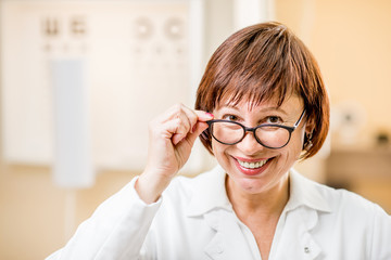 Close-up portrait of a senior woman doctor in uniform wearing eyeglasses in the ophthalmologic office