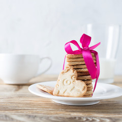 Cookies of shape heart with pink ribbon and milk on wooden table