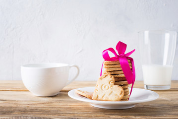Cookies of shape heart with pink ribbon and milk on wooden table