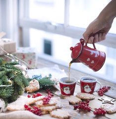a coffee pot in his hands pours coffee, berries and cookies, gifts, near a Christmas tree on a wooden table near the window