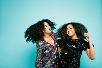 Laughing girls in fashion clothes dancing at blue wall in studio