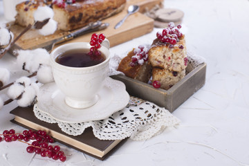 cup of tea and saucer, cupcake with red currant on wooden board and white background, cotton flowers