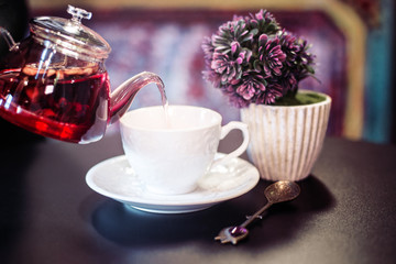 Fruit tea pouring to a white elegant cup, purple background, vintage spoon