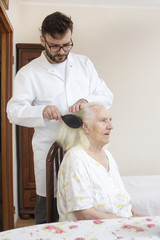 Pielęgniarz rozczesuje włosy starej kobiety siedzącej na krześle.