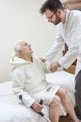Fototapeta premium Pielęgniarz pomaga podnieść się z lóżka starej kobiecie.