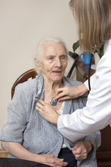 Lekarka w białym kitlu bada stetoskopem bardzo starą kobietę. 