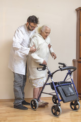 Pielęgniarz pomaga staruszce przy chodzeniu przy pomocy chodzika, balkonika. - obrazy, fototapety, plakaty