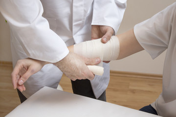 Dłonie lekarza zakładają opatrunek z bandaża na przedramie kobiety