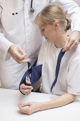 Pielęgniarz zakłada temblak na chorą zabandażowaną rękę kobiety.