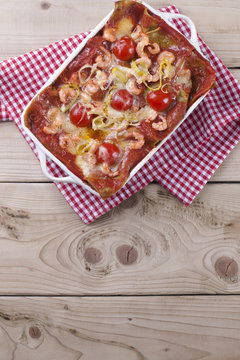 asagna baked in a white baking sheet, on a napkin in a red cage and wooden background