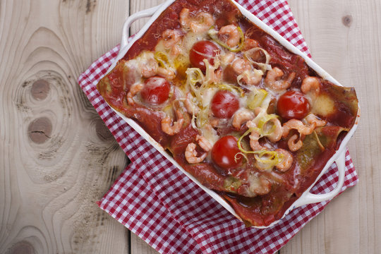 asagna baked in a white baking sheet, on a napkin in a red cage and wooden background