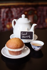 Kitchen tea time composition: white porcelan teapot, a cup with green tea and a muffin