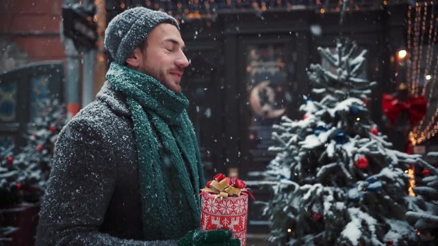 Young man walk city Christmas time hold present happy leisure looking smile handsome lifestyle building casual cool fashionable positive steadicam winter snow