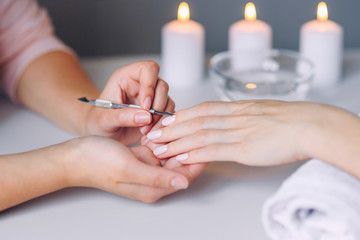 Nail care. Closeup of beautiful woman hands getting manicure in spa salon. Female manicurist cleaning cuticle with professional manicure pusher tool. Cosmetic procedure.