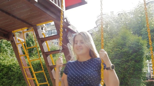4k video of beautiful smiling woman riding on swing at playground at sunny day