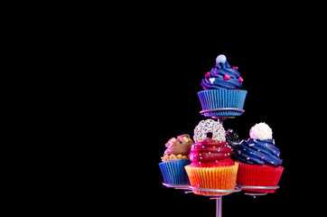 Tasty colorful cupcakes, on display stand, black background - copy space